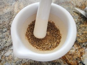Grinding coriander seeds with a mortar and pestle